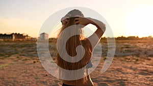 Woman in bikini swimsuit ruffles her long hair against setting sun on beach