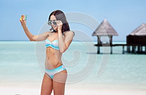 Woman in bikini taking smatphone selfie on beach