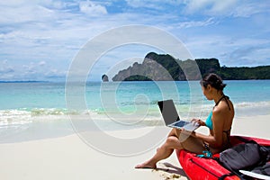 Woman in bikini using laptop at the beach