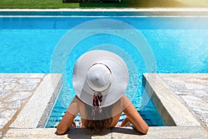 A woman in bikini and with white hat is relaxing in a swimming pool