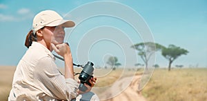 Woman with binoculars enjoying a beautiful view of the African savannah during a safari tour in Tanzania and Kenya