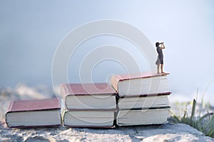 Woman with binoculars on the top of a ladder of books, surreal concept