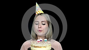 Woman in a birthday cap blows out the candles on the cake