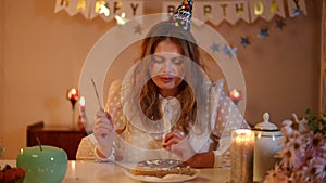 A woman in a birthday-cap licks the knife she used to cut the cake. A woman licks her lips while looking at the cake and
