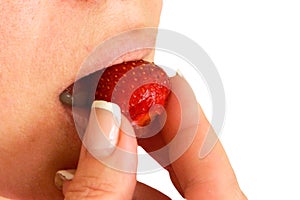 Woman bites and eats strawberry closeup image. Part of face with mouth and lips. Red berry is in fingers with clear nails.