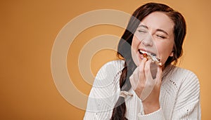 Woman biting a gingerbread Christmas cookie on a yellow background.