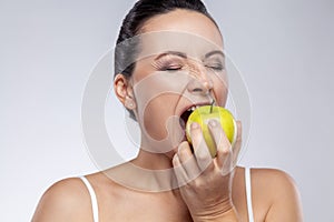 Woman biting green apple, uses natural cosmetic, healthy eating, vitamins for health and skin care.