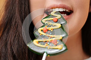 Woman biting off a Christmas tree lollipop with white healthy teeth.