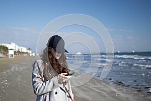 Woman in a black cap is using smartphone near the sea