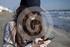 Woman in a black cap is using smartphone near the sea