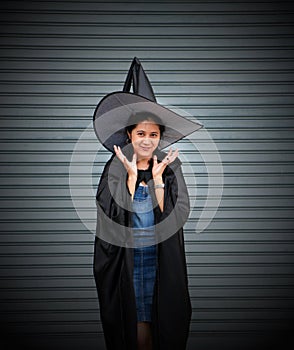 Woman with black cape and witch hat place two hands under her face on stripe metal background