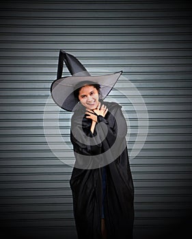 Woman with black cape and witch hat use her hands to strangle her neck on stripe metal background photo