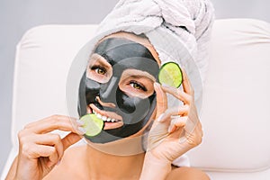 Woman with black charcoal facial mask and cucumber slices. Beauty treatments