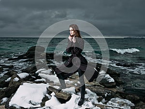 woman in a black coat outdoors landscape ocean dark clouds gothic