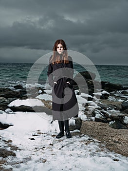 woman in a black coat outdoors landscape ocean dark clouds gothic