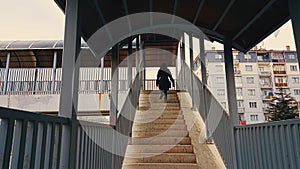 Woman with black coat walking up the stairs of the footbridge