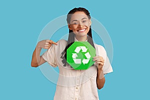 Woman with black dreadlocks pointing at green recycling symbol in her hands, ecology concept.