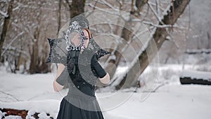 Woman in black dress in fairy tale image stands in snow in winter forest