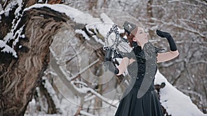 Woman in black dress in fairy tale image stands in snow in winter forest