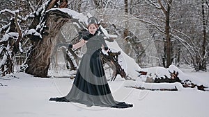 Woman in black dress in fairy tale image stands in snow in winter forest