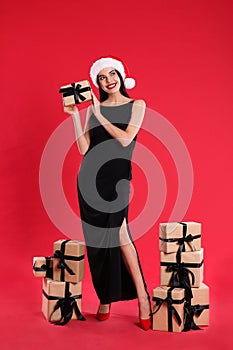 Woman in black dress and Santa hat with Christmas gifts on red background