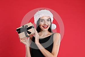 Woman in black dress and Santa hat holding Christmas gift on red background