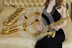 Woman in black dress sits with sax on bed with photo