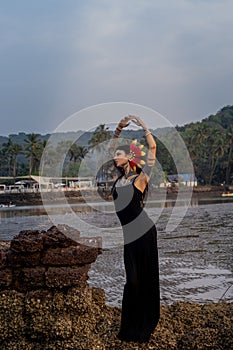 a woman in a black dress is standing on a rock near the ocean