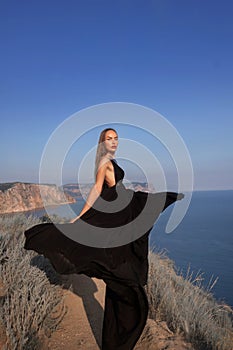 woman in black dress stands looking into the sea on a rock