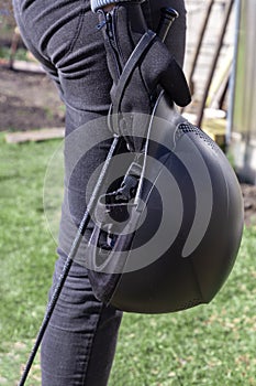 Woman in black gloves holding horse back riding helmet and whip in her hands.