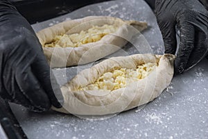 Woman in black gloves holds raw khachapuri. Process of making bakery. Adjarian Khachapuri Recipe Ã¢â¬â Georgian cheese bread