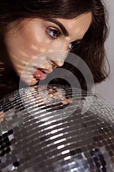 Woman with black hair holding disco ball showcasing fashion and beauty