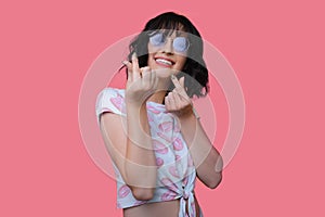 woman with black hair and nice sunglasses isolated over pink background gesturing money with her fingers