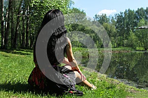 Woman with black hair sitting back to nature.