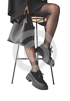 Woman with black handbag in hands sitting on chair, close-up to the legs in black pantyhose, isolated on a white