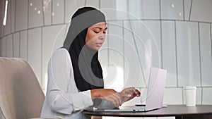Woman in black hijab having wrist pain caused by continuous work on laptop