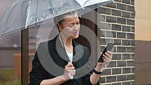 A woman in a black jacket under a transparent umbrella, on the street of the city, outdoors. Rain.