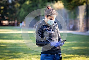 A woman in a black leather jacket and purple latex protective gloves holds a smartphone