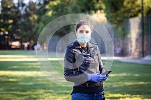 A woman in a black leather jacket and purple latex protective gloves holds a smartphone