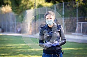 A woman in a black leather jacket and purple latex protective gloves holds a smartphone