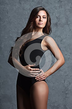 Woman in black leotard posing on grey background