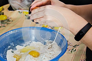 Woman with black manicure cooking and breaking eggs into a blue bowl of flour to make dough