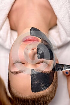 Woman with black mask on face close-up, top view. Spa treatments, beauty concept