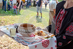 Woman in black national blouse embroidered with red and white threads holds tray with traditional Ukrainian food borscht