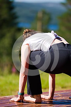 Woman with black pants and white t-shirt practicing Anjaneyasana yoga pose on the wooden ground