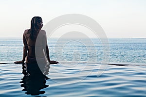 Woman black silhouette at infinity swimming pool