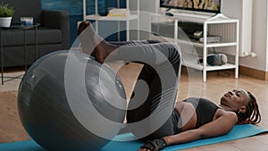 Woman with black skin training abs on swiss ball in living room