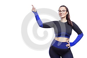 A woman in a black sports uniform points her finger up. Cute smiling brunette in glasses with a feminine figure. Activity, sport