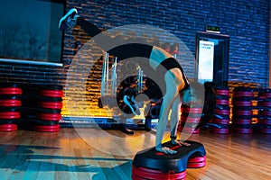 Woman in black sportswear doing aerobic exercise using step platform at gym.