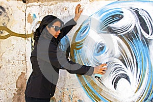 Woman in black spraying at a graffiti brick wall